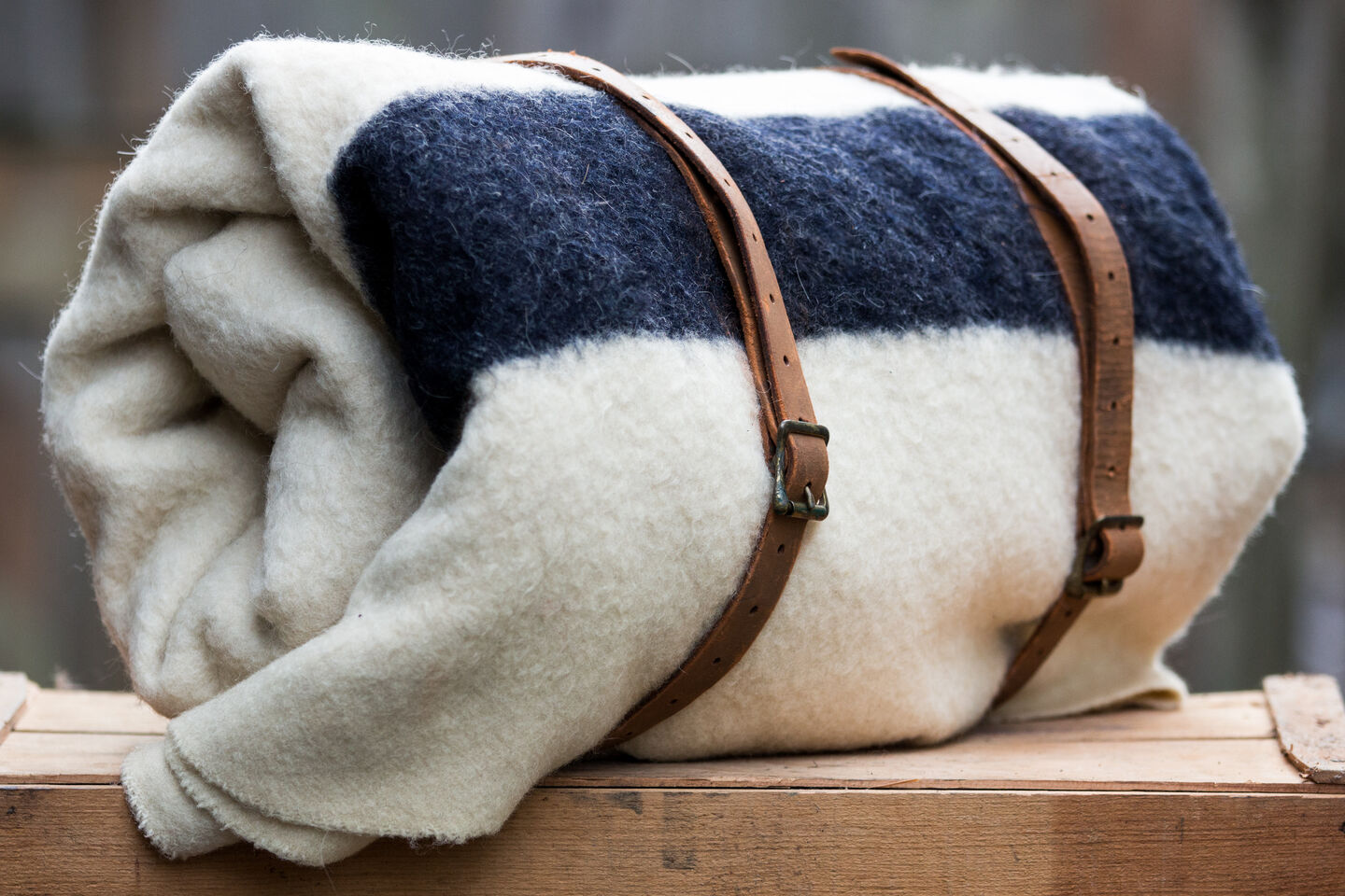 A close-up of a white blanket with a dark blue stripe rolled up and held together with brown leather straps.